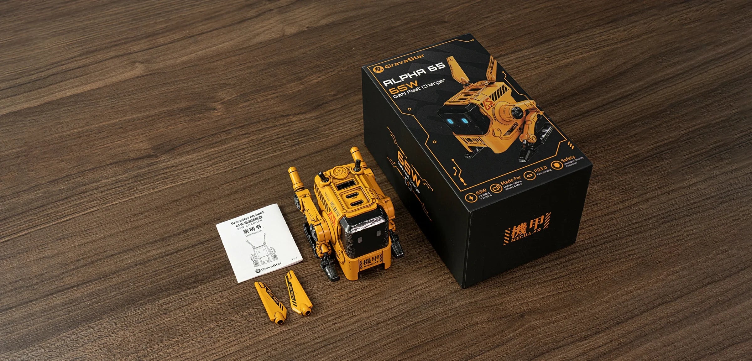 GravaStar Alpha65 GaN 65W Wall Charger War-Damaged Yellow packaging box studio view displaying handcrafted weathered yellow robot body, dual antennas, UK and EU plug adapters, and user manual.