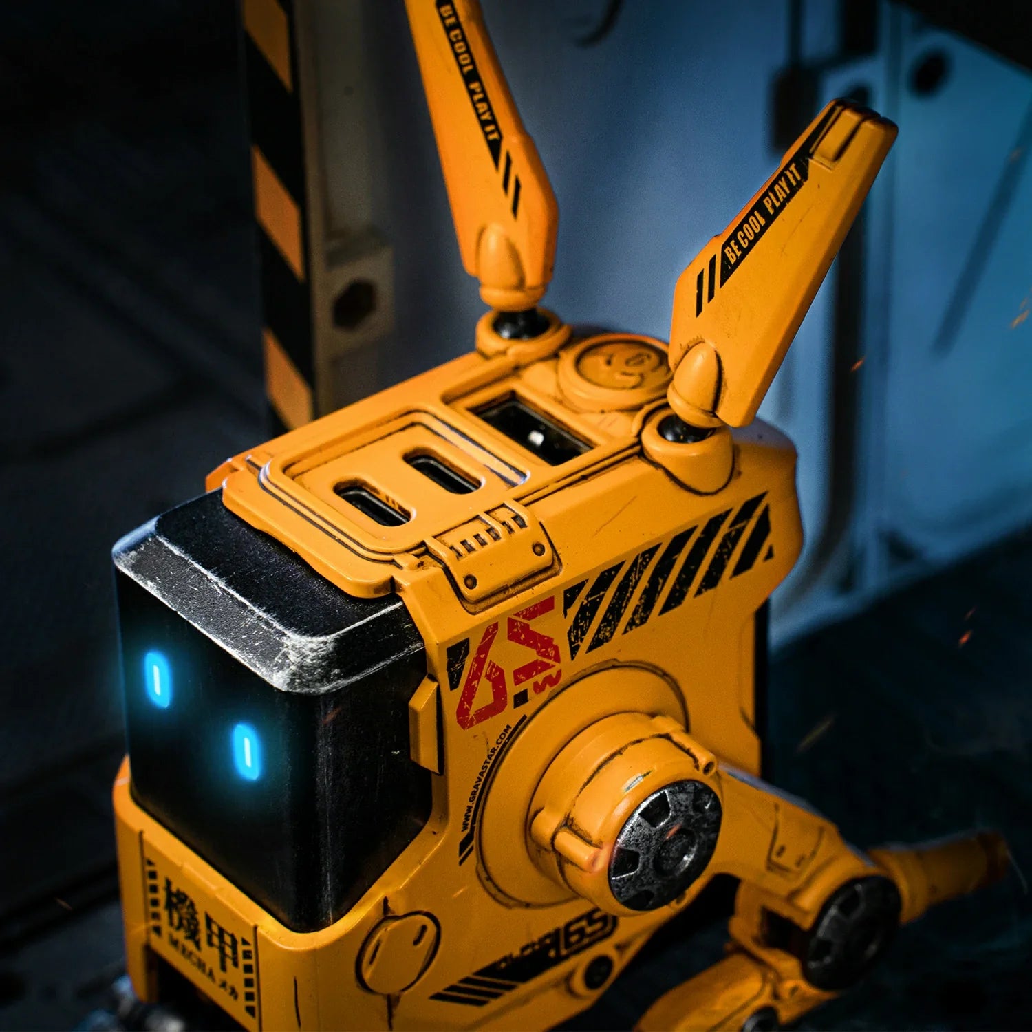 GravaStar Alpha65 GaN 65W Wall Charger War-Damaged Yellow top close-up view showing 3 USB ports (2 USB-C PD + 1 USB-A), handcrafted weathered yellow chassis, tactical antennas with BE COOL PLAY IT slogan, and ice blue RGB eyes.