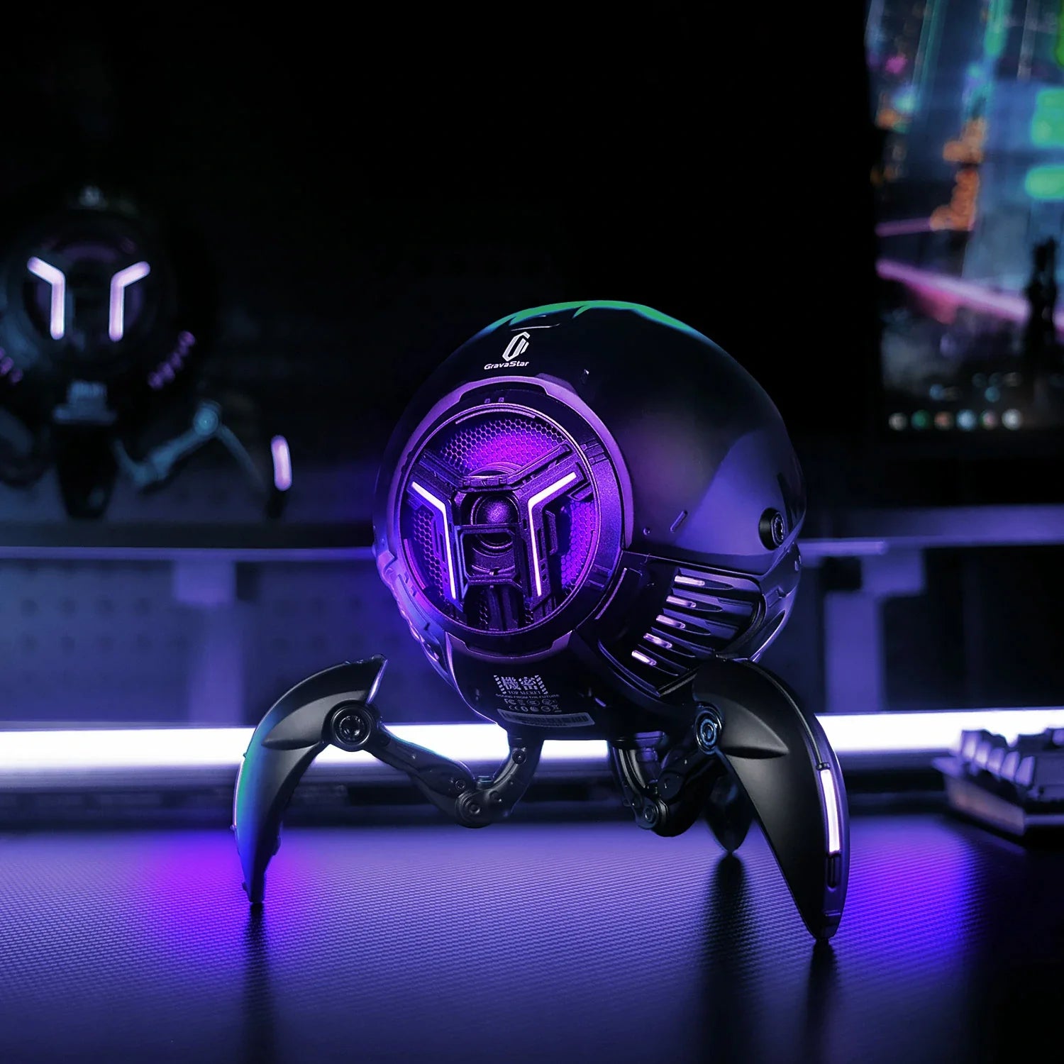 GravaStar Mars Pro Black Bluetooth speaker desktop setup view featuring matte black zinc alloy shell, shock-absorbing tripod legs, 20-watt dual speaker system with passive bass radiator, and dynamic neon RGB lighting effect.