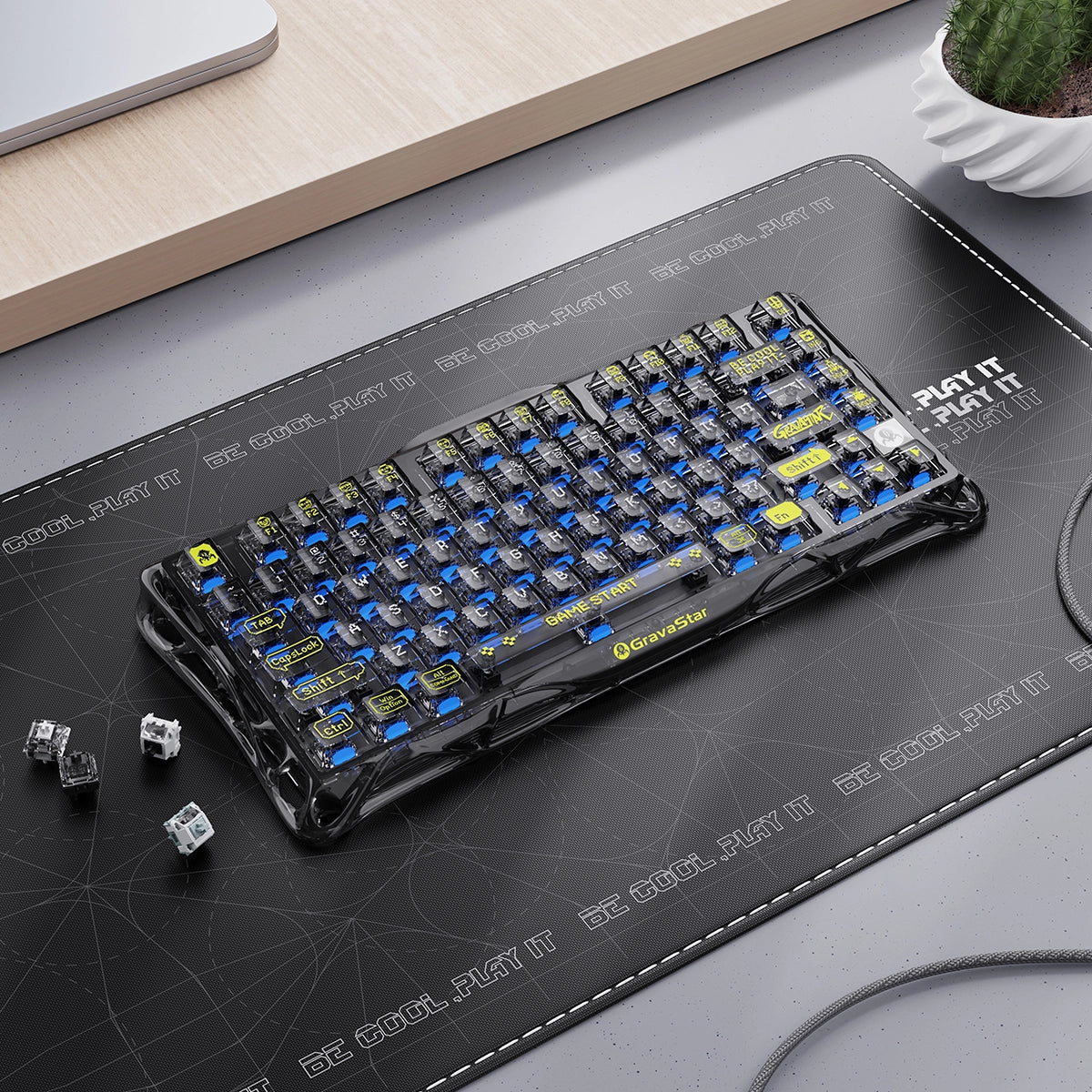 GravaStar Mercury K1 Lite Transparent Black – Desk setup view featuring 75% wireless mechanical gaming keyboard with coiled aviator cable, extra switches, clear PC housing, and immersive RGB backlight.