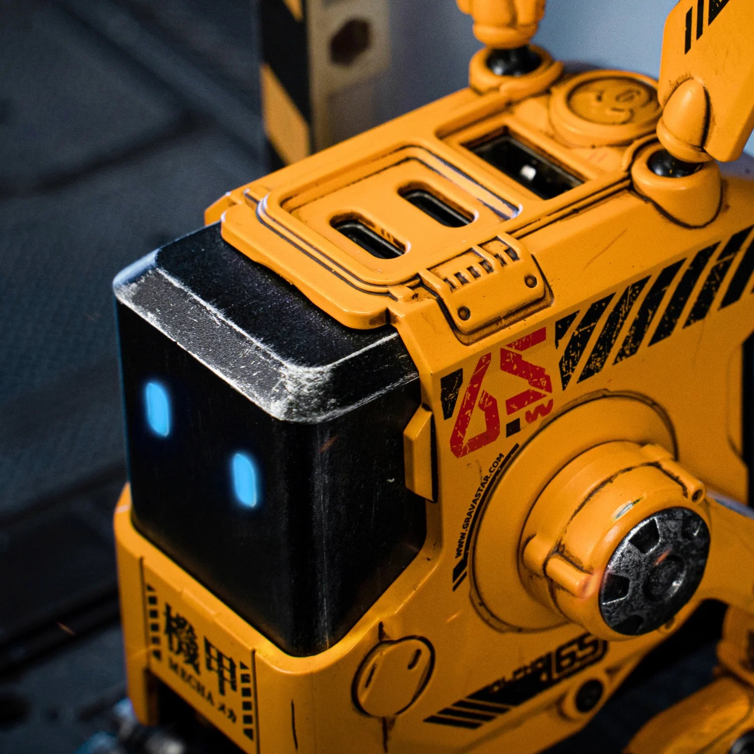 GravaStar Alpha65 GaN 65W Wall Charger War-Damaged Yellow macro close-up view showcasing handcrafted weathered distress finish, metallic edge wear, MECHA logo, ALPHA65 markings, and ice blue RGB eyes.