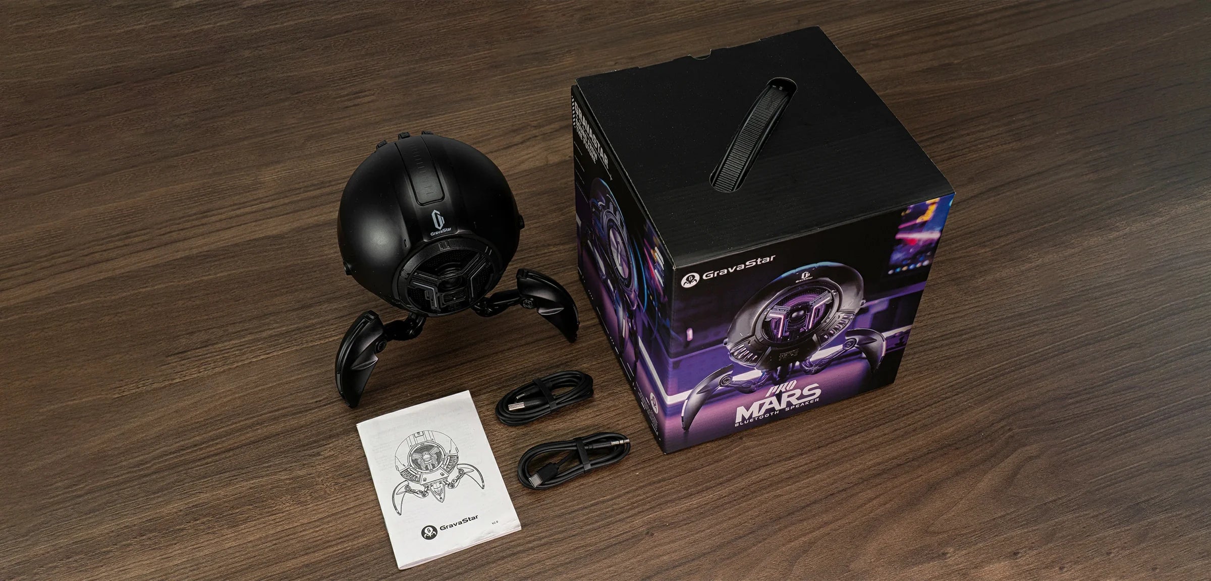 GravaStar Mars Pro Black Bluetooth speaker in-the-box accessories diagram featuring matte black zinc alloy speaker, Type-C charging cable, Type-C to Aux audio cable, official packaging box, and user manual.