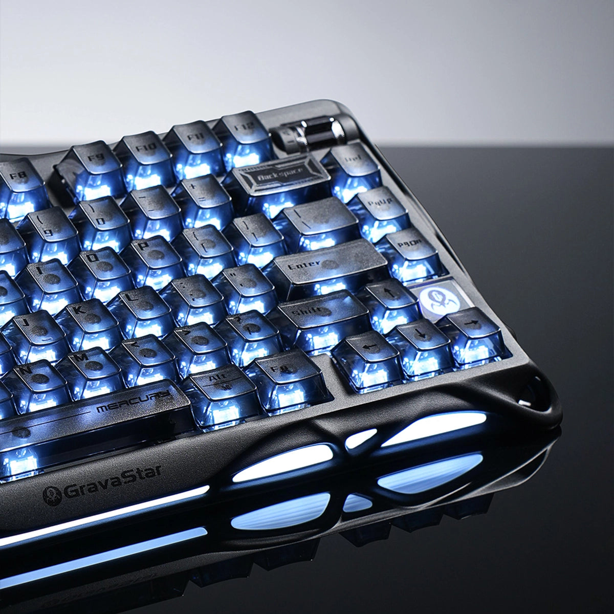 GravaStar Mercury K1 Stealth Black 75% wireless mechanical gaming keyboard close-up showcasing hollowed matte black aluminum alloy exoskeleton frame, engraved GravaStar logo, translucent PBT keycaps, and dual-zone ice blue RGB backlighting.
