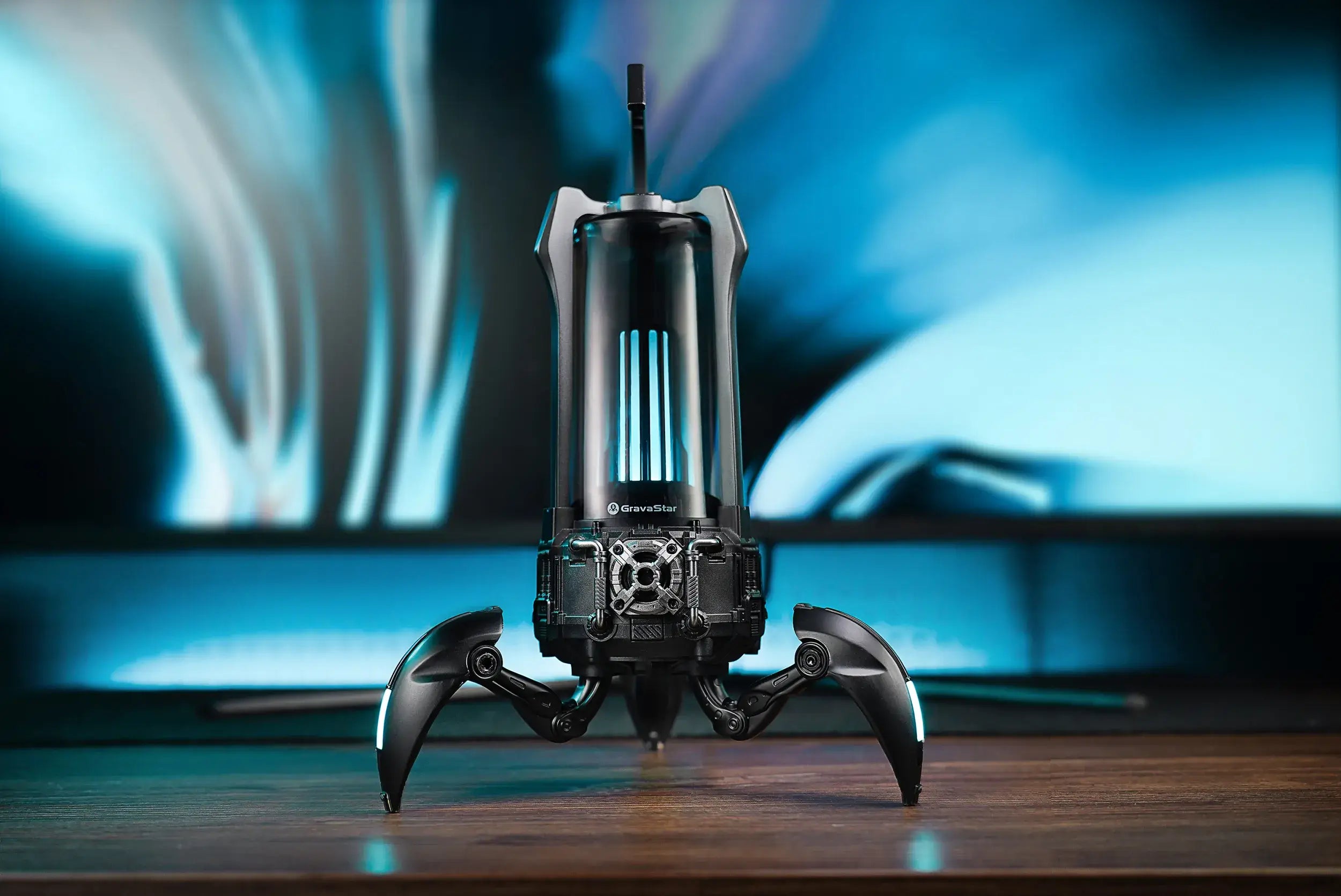 GravaStar Supernova Matt Black mecha lantern Bluetooth speaker on wooden desk featuring 25W dual-driver sound system, 3-inch woofer, 0.5-inch tweeter, zinc alloy frame, foldable tripod stand, carry handle, and dynamic blue RGB lighting.