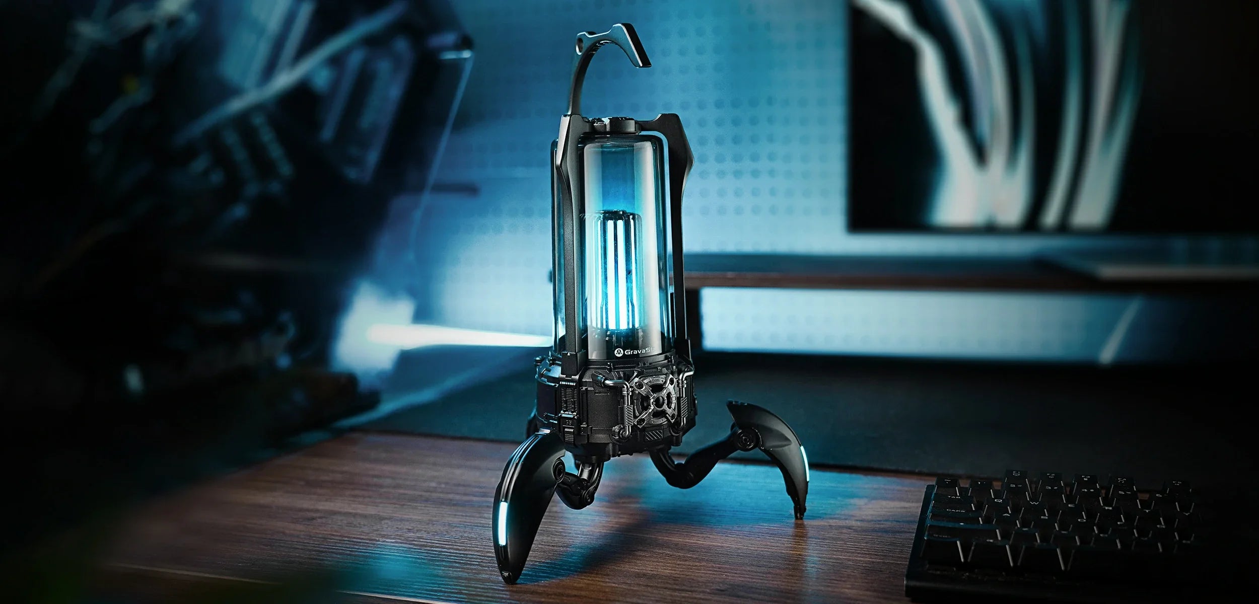 GravaStar Supernova Matt Black mecha lantern Bluetooth speaker full width setup banner featuring 25W dual-driver sound system, zinc alloy frame, 3-legged tripod stand, top handle, and ice blue RGB lighting alongside gaming keyboard.
