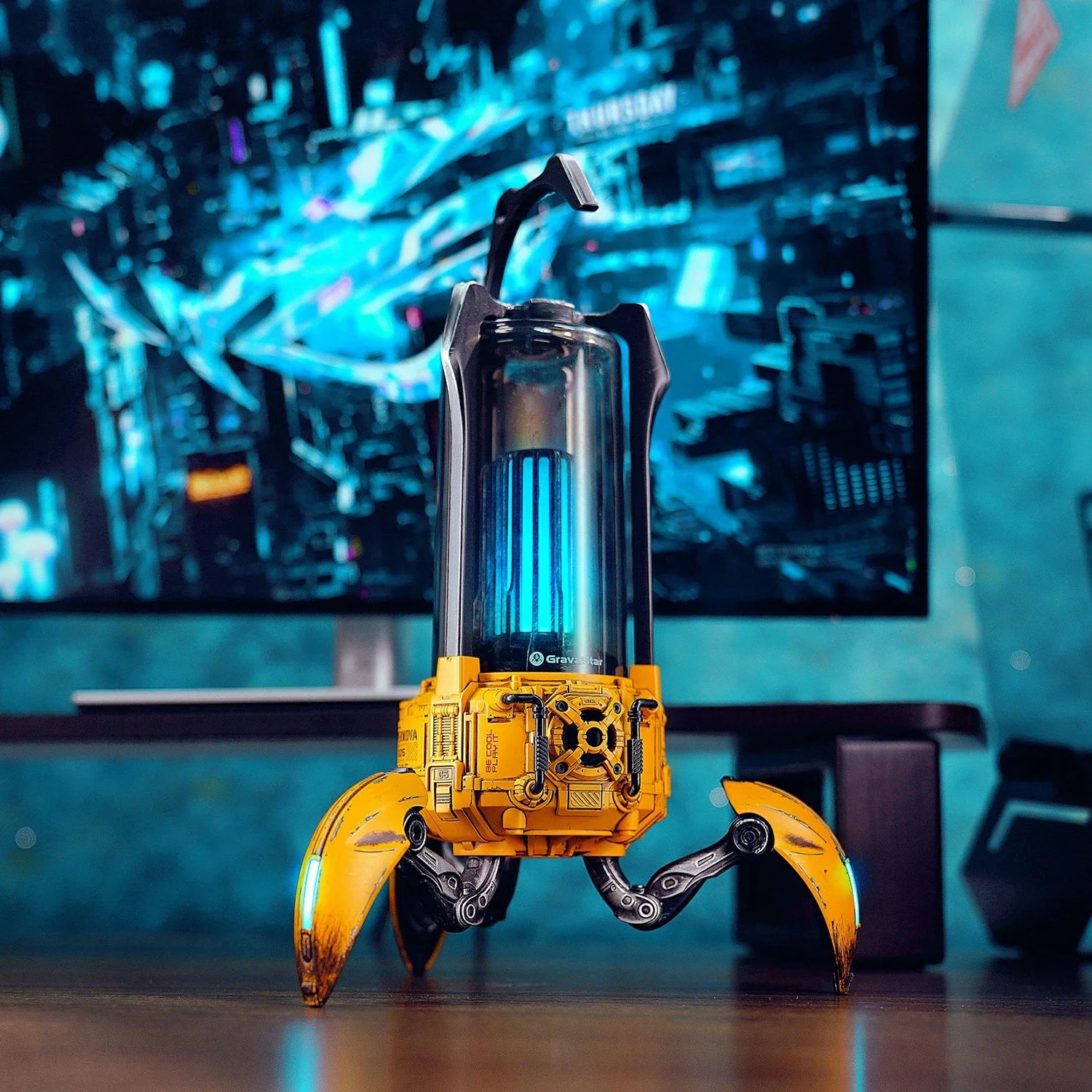 GravaStar Supernova War Damaged Yellow handcrafted mecha lantern Bluetooth speaker on gaming desk featuring 25W dual-driver sound system, zinc alloy chassis, top carry handle, foldable tripod stand, and ice blue RGB lighting.