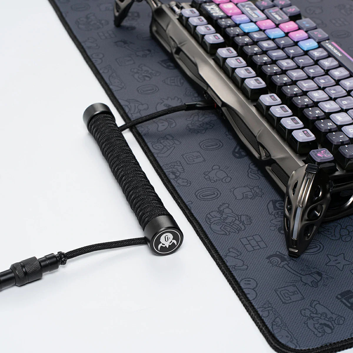 GravaStar Coiled Aviator USB Cable in black studio desktop setup view connected to Mercury K1 Pro keyboard, featuring 4-pin nickel-plated aviator connector, TPU EVA double-sleeved braided cable body, and GravaStar tactical logo emblem ring, perfect paired with Mercury K1 Pro keyboard and GravaStar Gaming Mouse Pad.