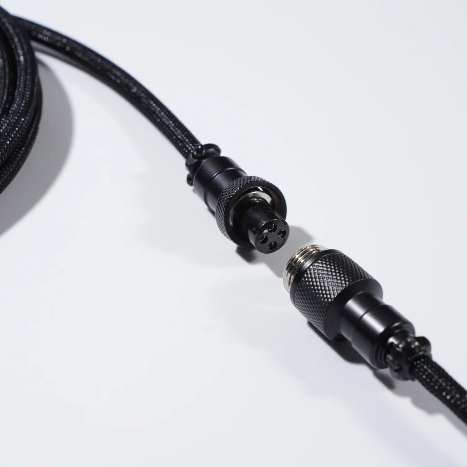 GravaStar Coiled Aviator USB Cable in black studio desktop top-down close-up view connected to Mercury K1 Pro keyboard, featuring 4-pin nickel-plated aviator connector, TPU EVA double-sleeved braided cable body, and GravaStar tactical logo emblem ring, perfect paired with Mercury K1 Pro keyboard and GravaStar Gaming Mouse Pad.