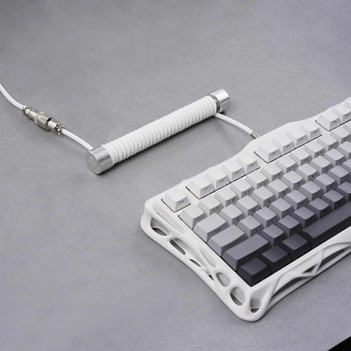 GravaStar Coiled Aviator USB Cable in white studio desktop setup view connected to Mercury K1 keyboard, featuring 4-pin nickel-plated aviator connector, TPU EVA double-sleeved braided cable body, and GravaStar tactical logo emblem ring, perfect paired with Mercury K1 Pro keyboard and GravaStar Gaming Mouse Pad.