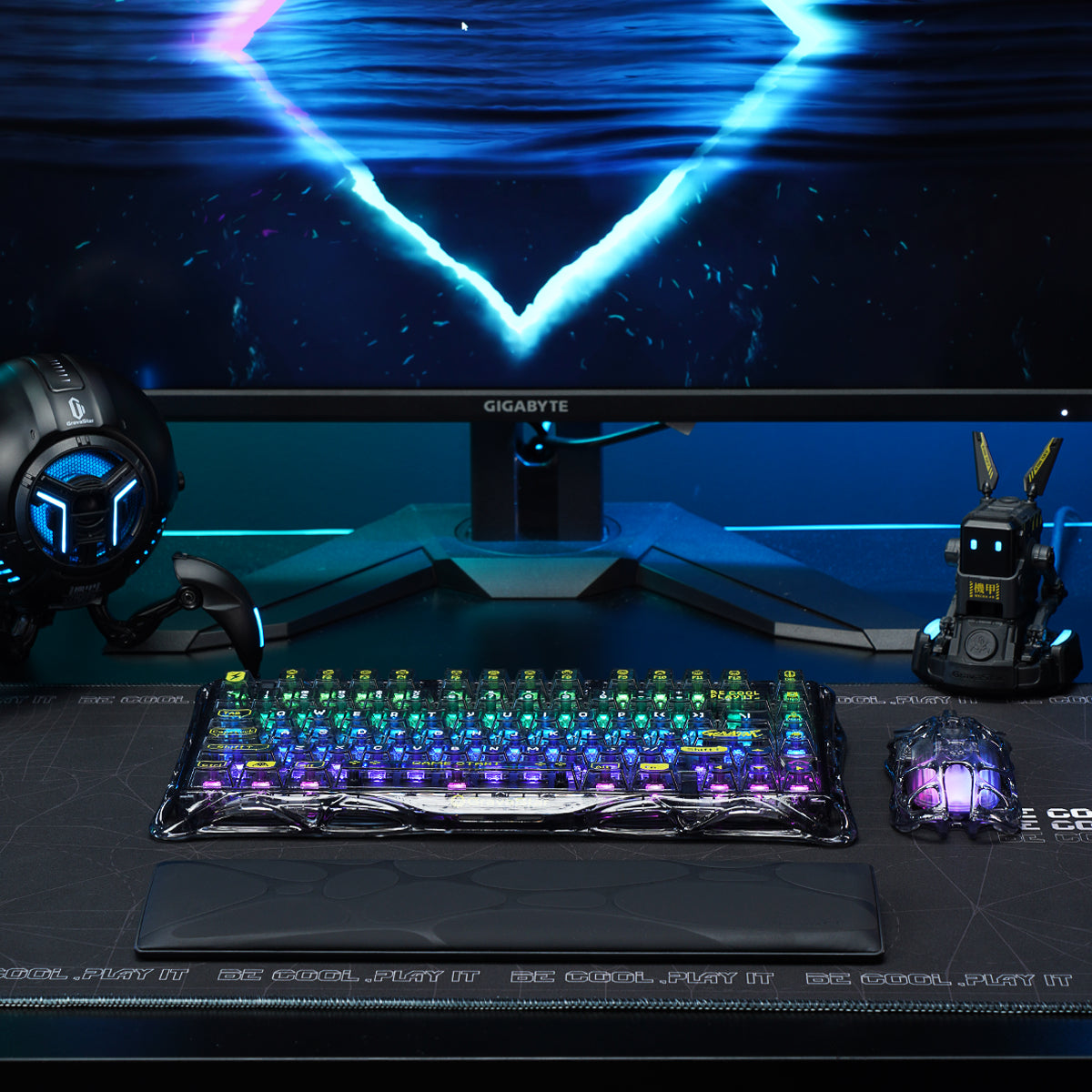 GravaStar Core Flex Gaming Set Transparent Black studio desk setup cyberstation view featuring Mercury K1 Lite 75% wireless mechanical keyboard with RGB lighting, Mercury M2 gaming mouse with PAW3395 sensor, and free bonus keyboard wrist rest pad, perfect paired with GravaStar Gaming Mouse Pad black deskmat and Mars Pro Black speaker.