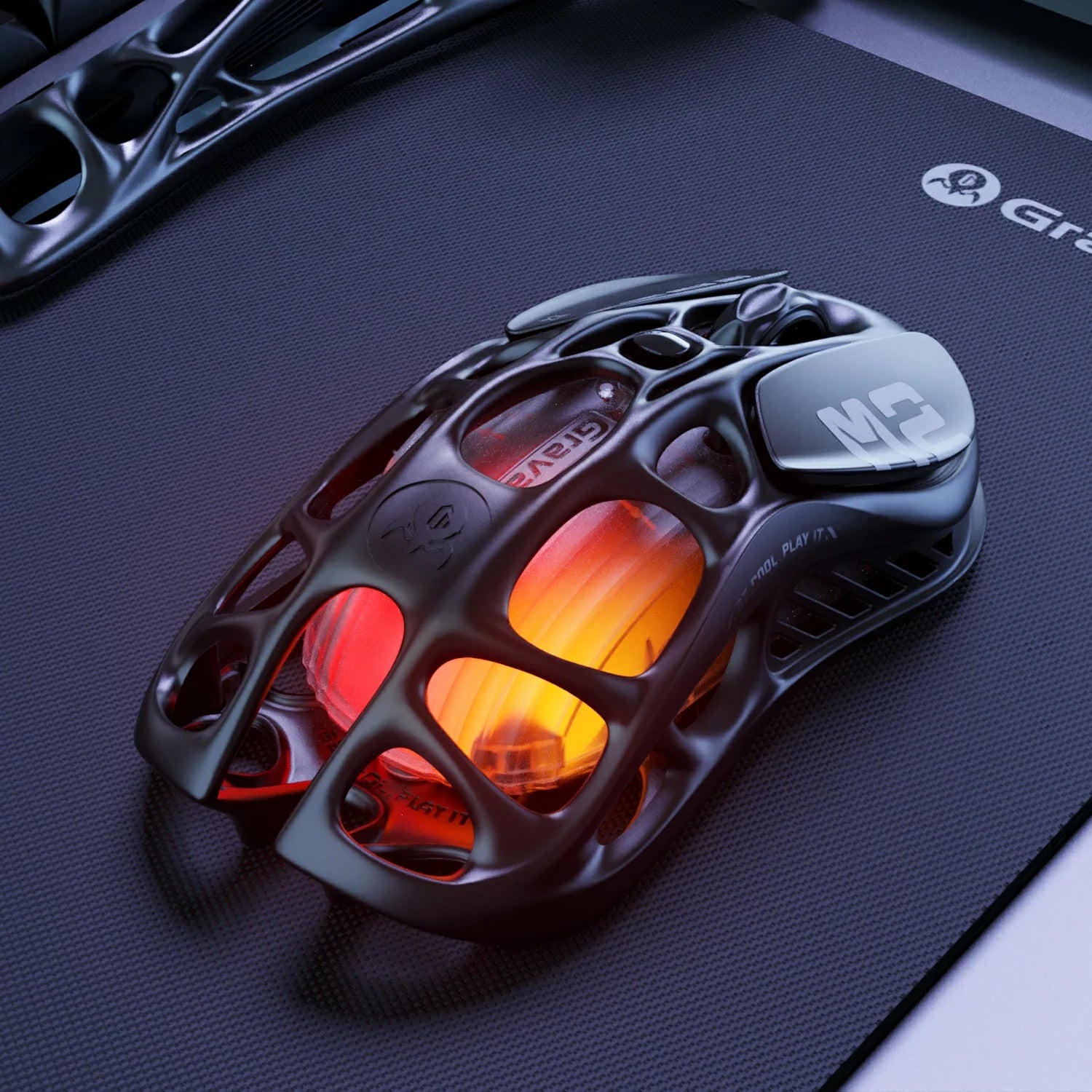 GravaStar Mercury M2 Stealth Black wireless gaming mouse shown on dark desk setup, featuring hollow skeletal frame design, PAW3395 26K DPI sensor, Kailh 80M micro-switches, 79g tactical layout, and customizable amber RGB lighting, perfect paired with Mercury K1 Stealth Black keyboard and Mars Pro Black speaker.